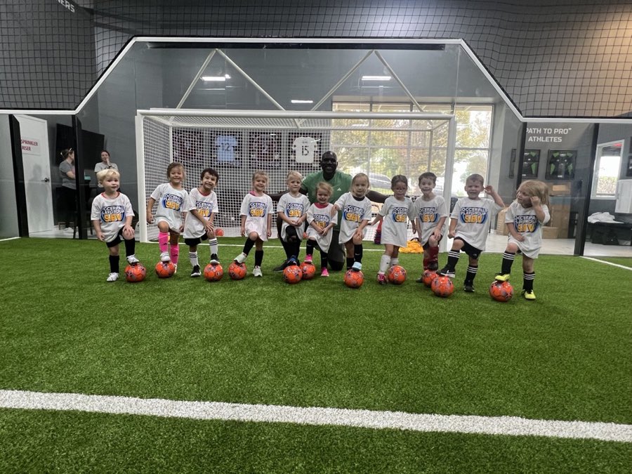 A group of Soccer Pals kids lined up with their soccer balls and their coach