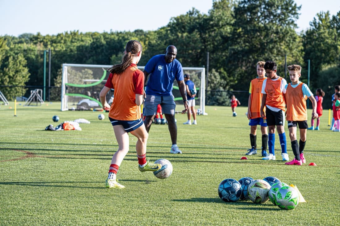 A PDP player dribbling past her coach while teammates in orange pinnies wait their turn